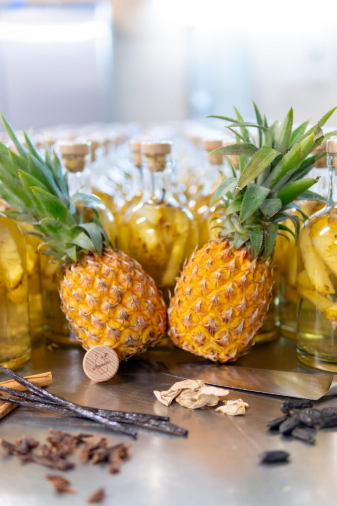 Bouteilles de rhum So'Rhumantic arrangé avec des ananas frais et des épices sur une table.