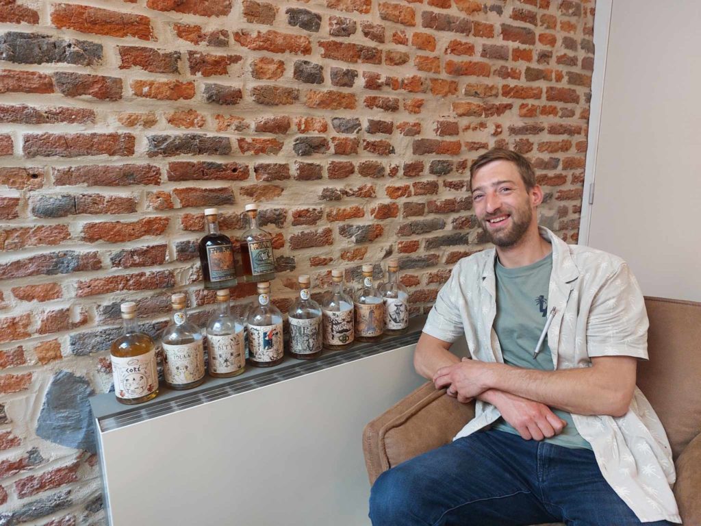 Le fondateur de New Yellow Poppy, posant avec une sélection de leurs rhums artisanaux uniques, devant un mur de briques.