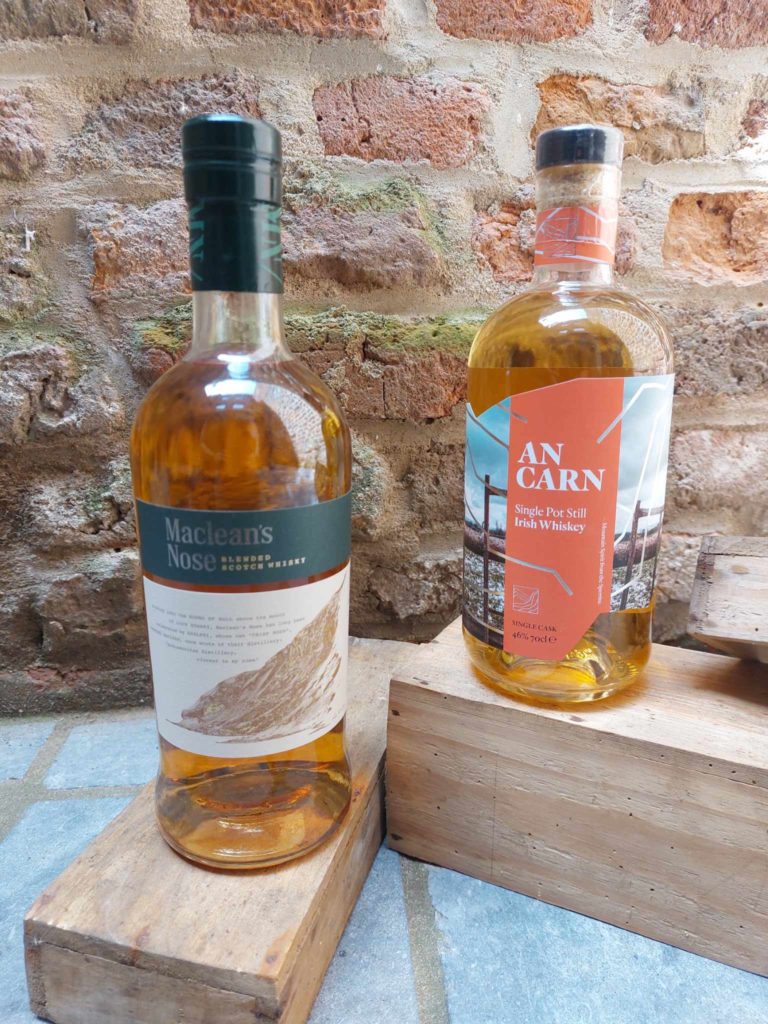 Deux bouteilles de whisky, Maclean's Nose et An Carn, posées sur des caisses en bois avec un mur en briques en arrière-plan.