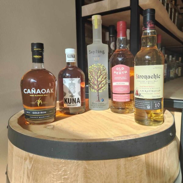 Assortiment de spiritueux premium, y compris du rhum, du gin et du whisky, exposés sur un tonneau en bois.