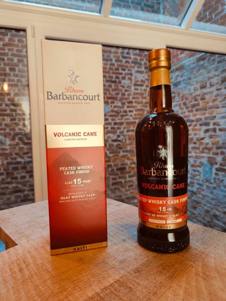 outeille de Rhum Barbancourt Volcanic Cane 15 ans et son étui rouge, posés sur une table en bois avec fond de mur en briques