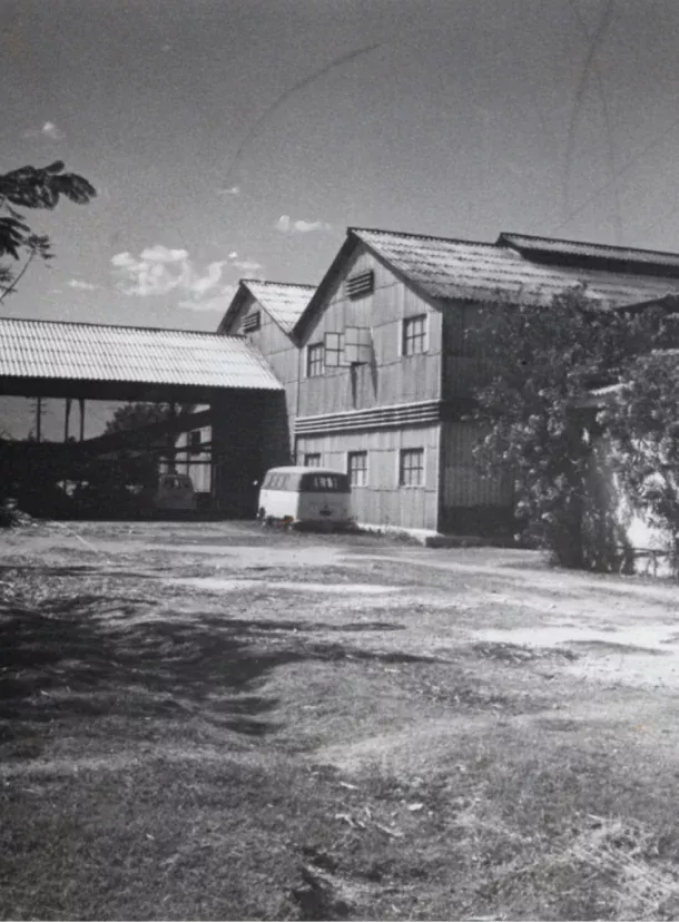 Photo en noir et blanc de la distillerie Barbancourt avec bâtiments en bois et fourgons d’époque